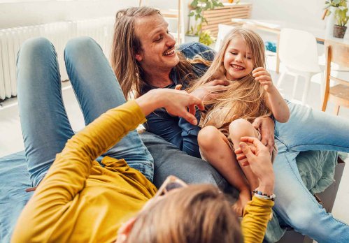 Familie sitzt mit ihrer kleinen Tochter auf der Couch und macht Quatsch
