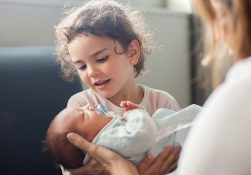 Kleines Mädchen sitzt im Krankenhaus und hält ein Baby im Arm