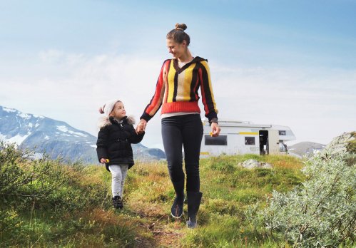 Mutter geht mit Tochter in den Bergen spazieren. Hinter ihnen steht ein Wohnmobil.