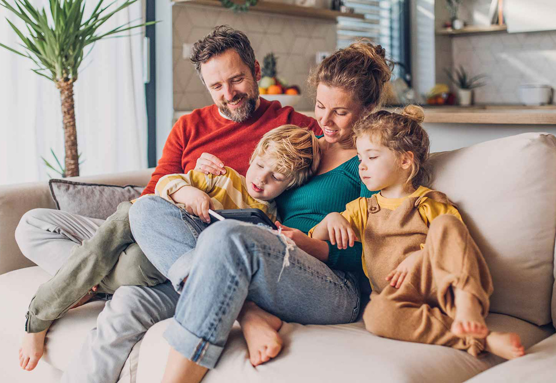 Familie mit zwei Kindern sitzt auf dem Sofa und schaut auf ein Tablet.