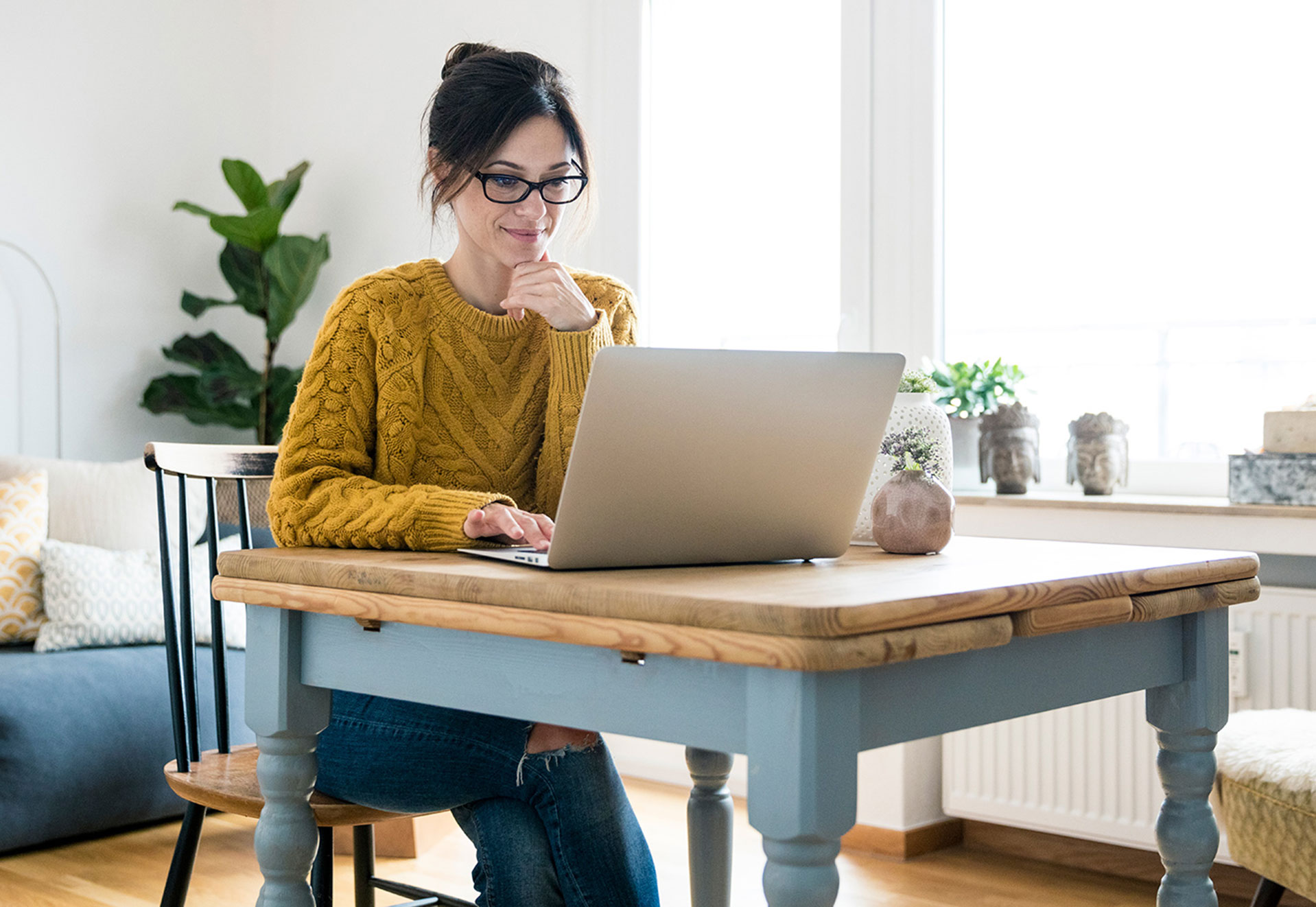 Frau mit gelbem Strickpulli und Brille sitzt vor einem Laptop.