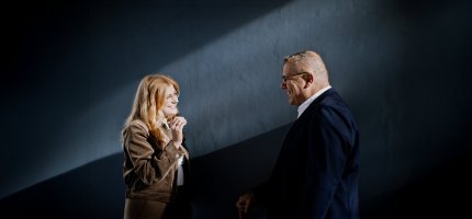 Mann und Frau stehen sich vor einer dunklen Wand gegenüber