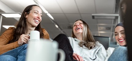 Personen sitzen entspannt mit Tassen in einem Büro.