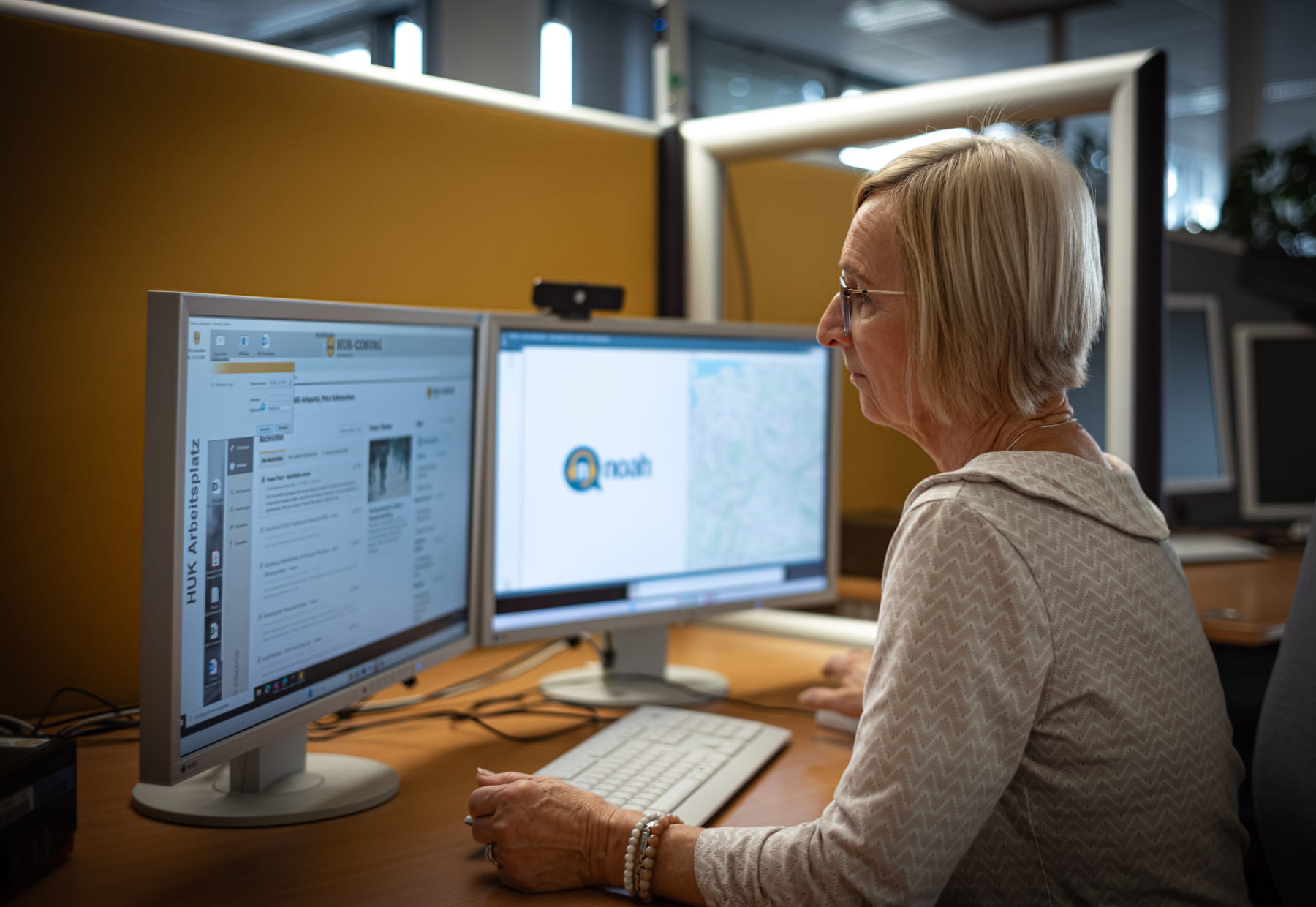 Eine Person arbeitet an zwei Monitoren in einem Büro. Auf den Bildschirmen sind Webseiten und Anwendungen geöffnet.