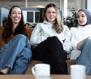 Drei Personen sitzen auf einem Sofa im Büro. Im Vordergrund stehen Tassen.