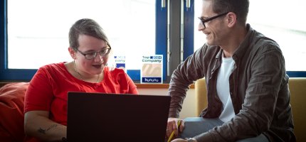Eine Frau mit Laptop und ein Mann sitzen nebeneinander und unterhalten sich
