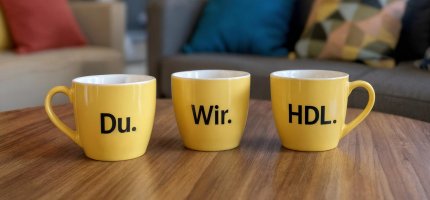 Drei Tassen mit der Aufschrift Du. Wir. HDL. stehen auf einem Tisch.