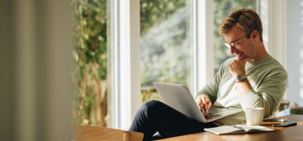 Eine Person sitzt an einem Tisch und arbeitet konzentriert an einem Laptop