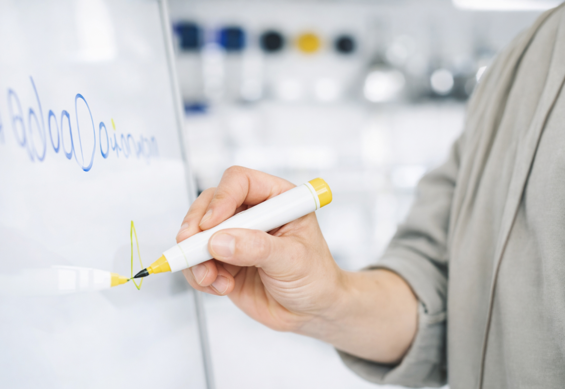 Eine Person schreibt mit einem gelben Marker auf eine weiße Tafel.