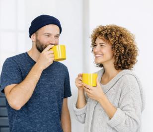 Zwei Personen trinken aus gelben Tassen und stehen nebeneinander.