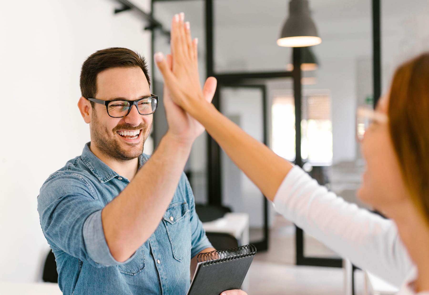 Zwei Personen geben sich ein High-Five in einem Büro. Eine Person hält ein Notizbuch.