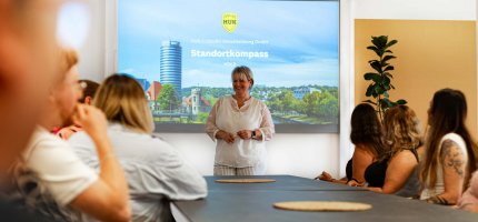 Frau hält Präsentation vor Leuten am Tisch