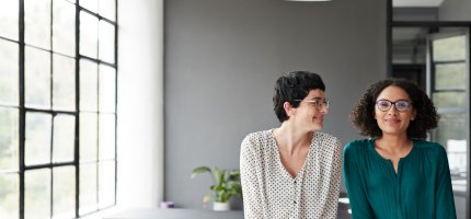 Zwei Frauen mit Brille und dunklen Haaren sitzen im Büro