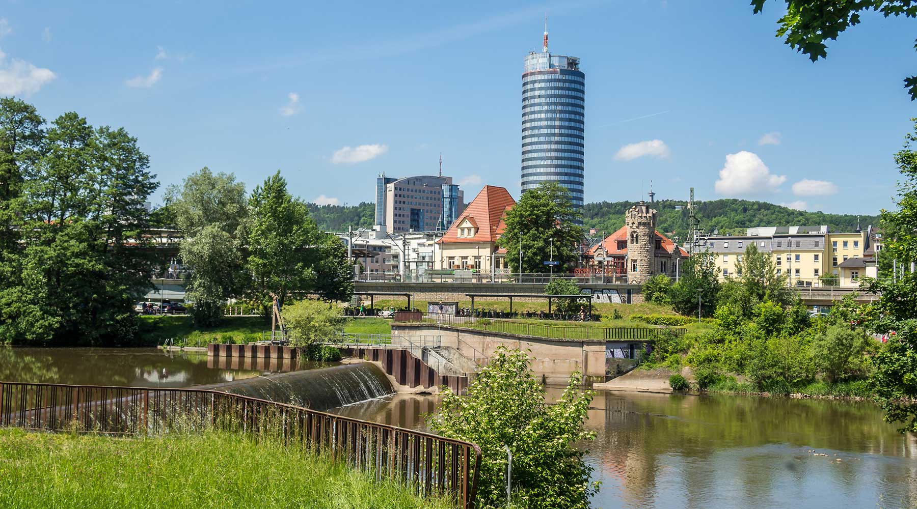 Die Skyline von Jena ist geprägt von einer interessanten Mischung aus moderner und historischer Architektur. Im Vordergrund der Fluss Saale und im Hintergrund der JenTower.