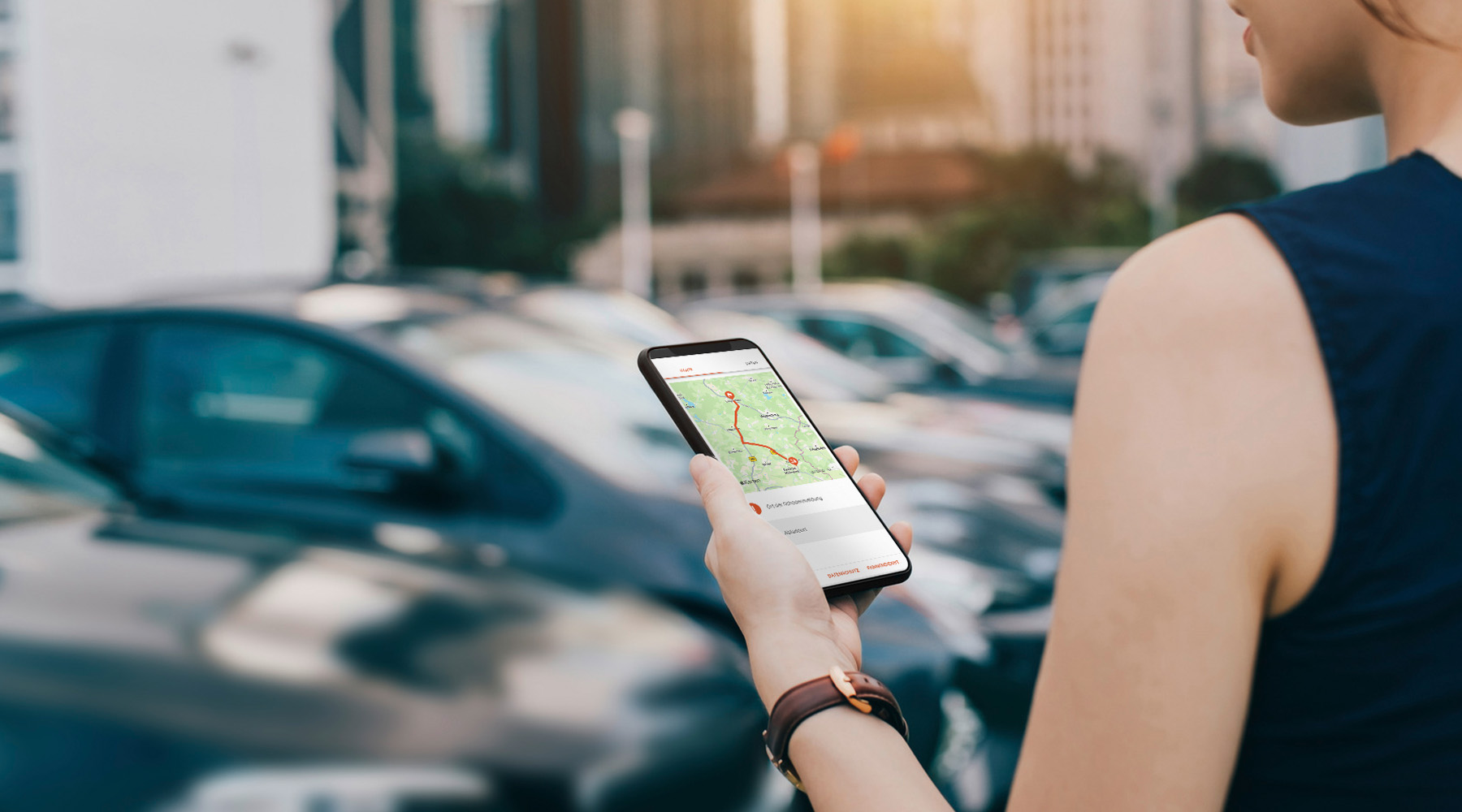 Frau steht mit Ihrem Handy in der Hand auf einem Parkplatz.