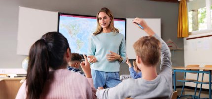 Eine Lehrerin unterrichtet Ihre Schüler. Im Hintergrund sieht man eine Weltkarte.