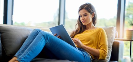 Junge Frau liegt mit Tablet entspannt auf dem Sofa