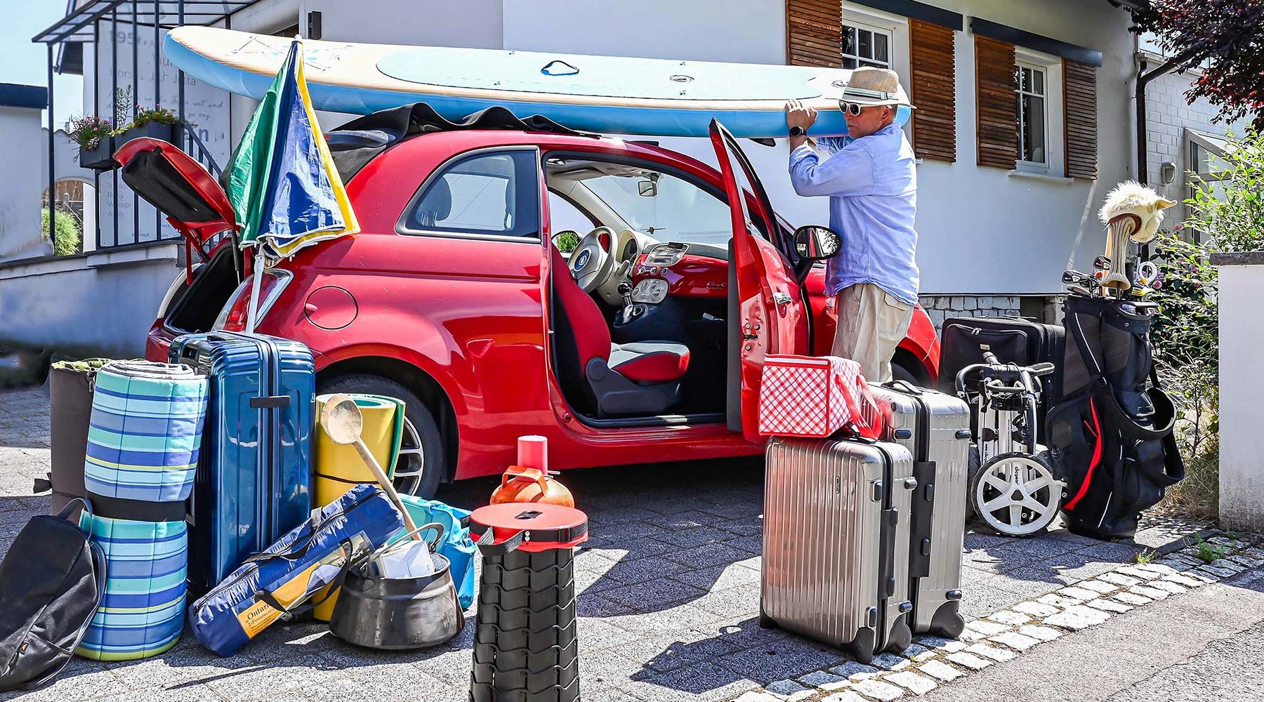 Mann versucht Gepäck wie Koffer, Sonnenschirm und Golfausrüstung in sein kleines Auto zu bekommen