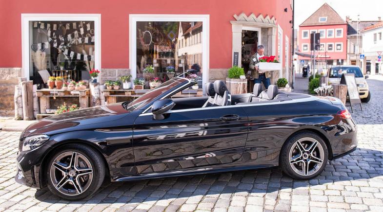 Schwarzes Cabriolet auf Kopfsteinpflaster vor rotem Gebäude.