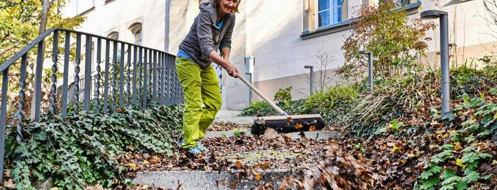 Frau kehrt Laub von der Treppe