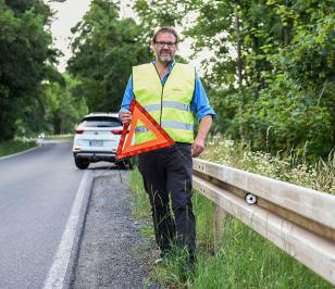 Mann mit Warnweste stellt das Warndreieck auf