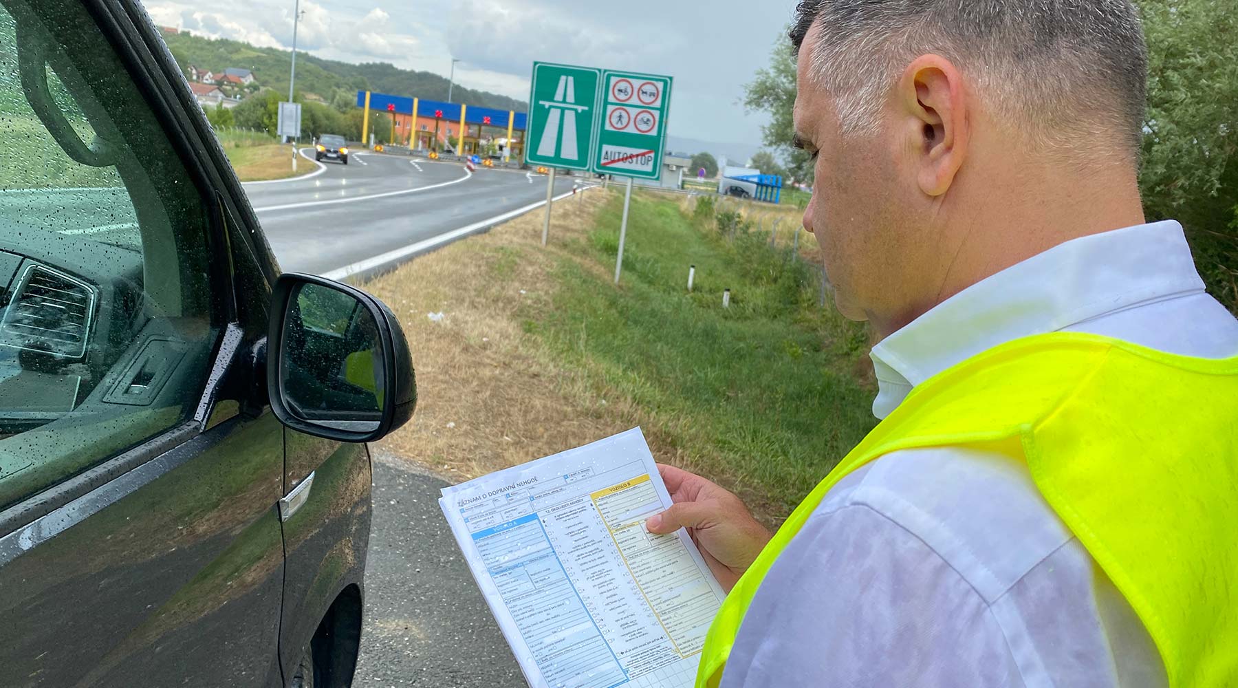 Mann steht mit einer Warnweste neben seinem Fahrzeug im Ausland