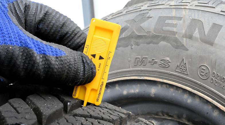 Das Bild zeigt eine Person, die mit einem gelben Messgerät die Profiltiefe eines Winterreifens überprüft. 