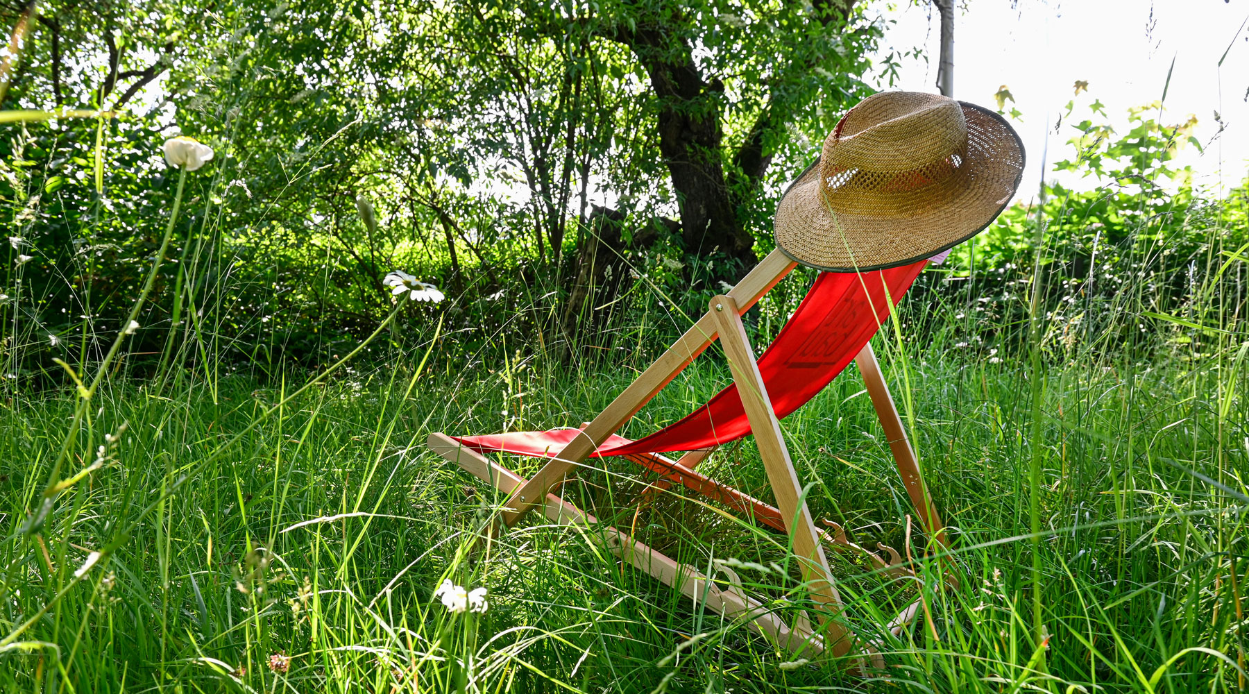 roter Liegestuhl mit Sonnenhut auf einer grünen Wiese