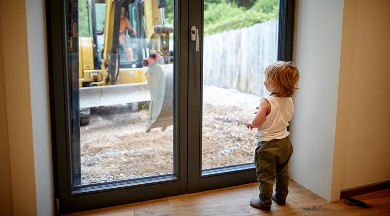 Ein kleines Kind steht schaut durch das Fenster auf die Baustelle.