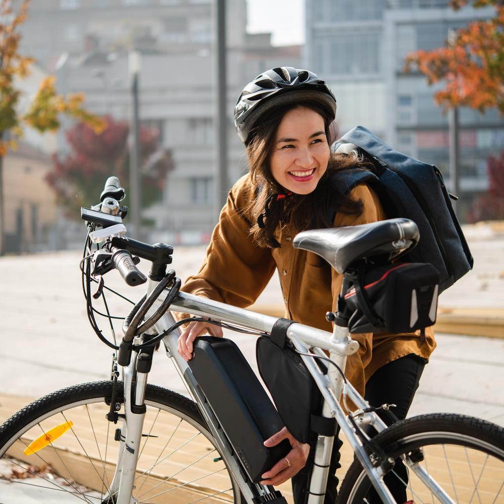 Junge Frau hat ihr E-Bike abgestellt und ist gerade dabei den Akku aus der Halterung zu nehmen.