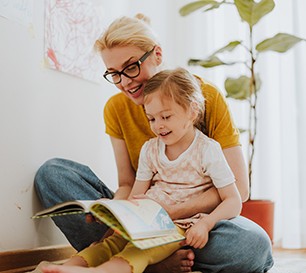 Eine Mutter hat ihre Tochter auf dem Schoß und liest aus einem Buch vor.