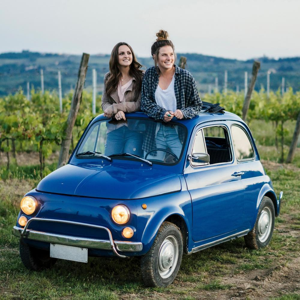 Zwei Touristinnen haben mit ihrem Auto in einem Weinberg angehlaten. Sie sind im Auto aufgestanden und schauen sich durch das offene Schiebedach die Landschaft an.