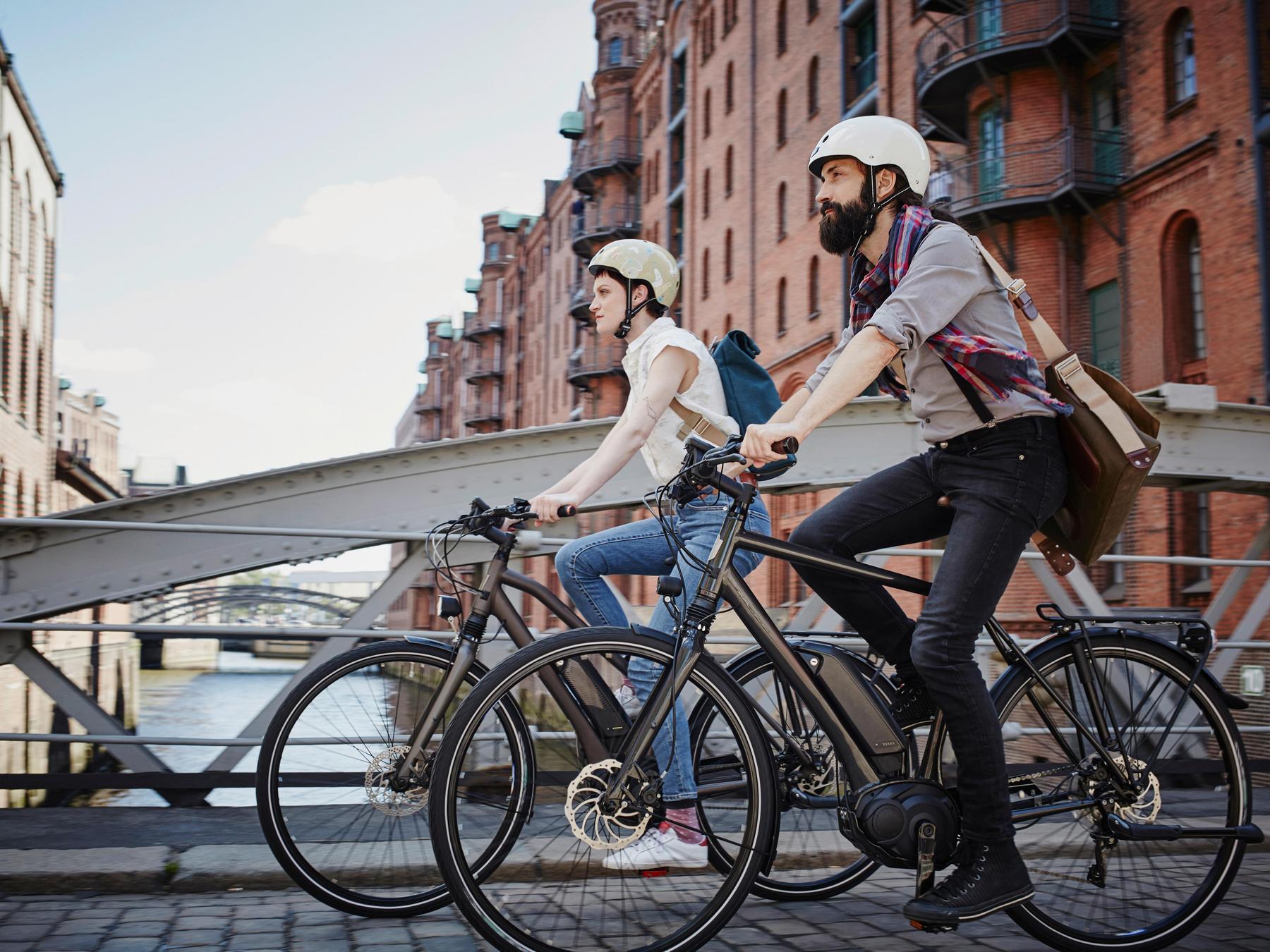 Paar auf E-Bikes fährt über eine Brücke.