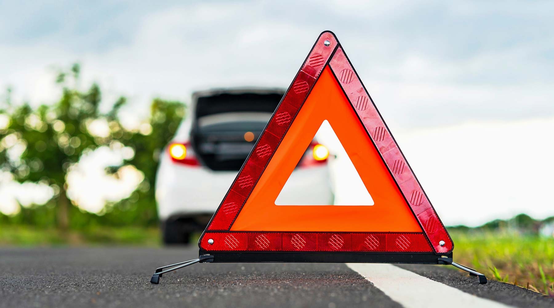 Warndreieck steht hinter weißem Auto.
