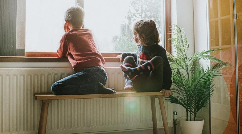 Zwei Kinder schauen Zuhause aus dem Fenster.