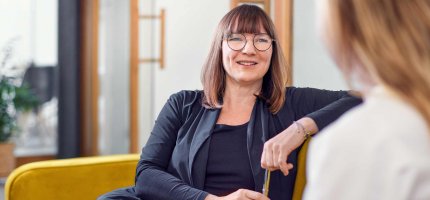 Zwei Frauen unterhalten sich sitzend in einem Büro.