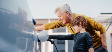 Opa und Enkelsohn laden ein E-Auto.