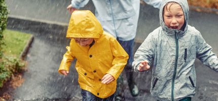 Drei Kinder rennen in Regenjacken durch den Regen