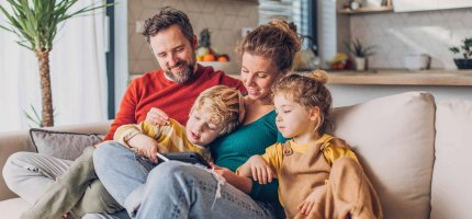 Familie mit zwei Kindern sitzt auf dem Sofa und schaut auf ein Tablet.