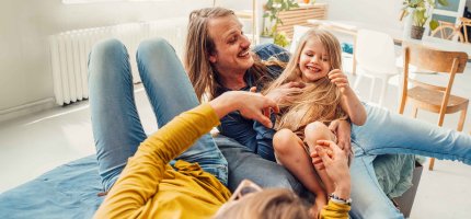 Mann tobt mit seinen beiden Kindern im Haus herum 