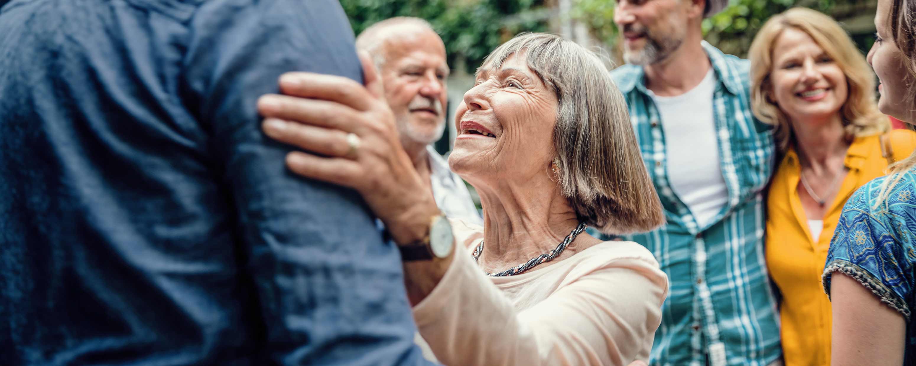 Alter Frau begrüßt einen Mann vor vier weiteren, älteren Personen.