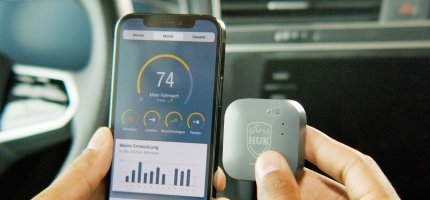 Ein Smartphone mit einer Telematik-App und einem Sensor zur Fahrdatenerfassung im Auto.
