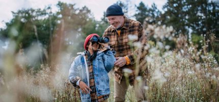 Junge steht mit seinem Opa in der Wiese und schaut durch ein Fernglas