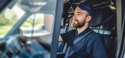 Ein Handwerker mit dunkelblauem Polo-Shirt und Kappe sitzt in seinem Lieferwagen.