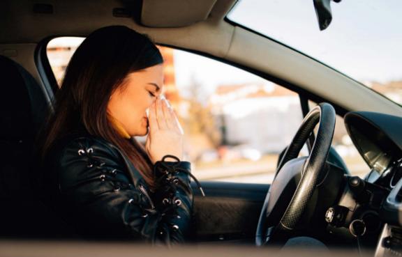 Frau sitzt in ihrem Auto und putzt sich die Nase