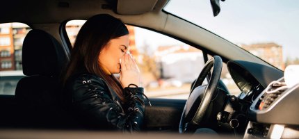 Frau sitzt in ihrem Auto und putzt sich die Nase