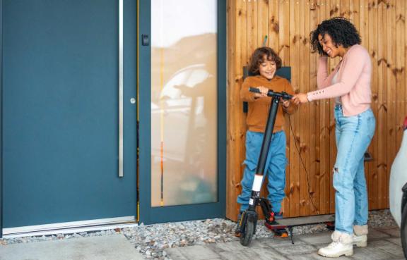 Mutter und Sohn stehen mit einem E-Scooter vor ihrem Haus