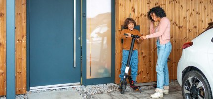 Mutter und Sohn stehen mit einem E-Scooter vor ihrem Haus