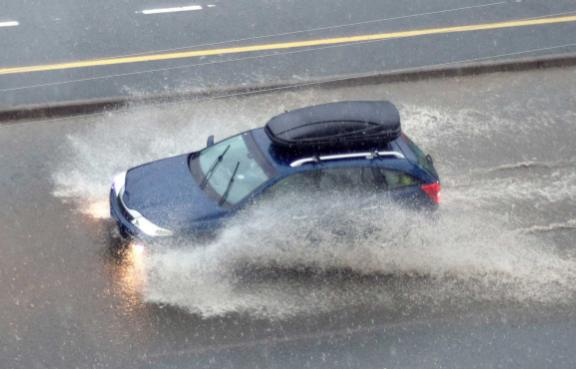 Ein Auto fährt durch das Wasser einer überschwemmten Straße.