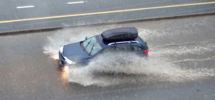 Ein Auto fährt durch das Wasser einer überschwemmten Straße.